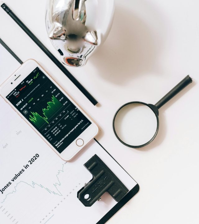 Flat lay of financial tools including smartphone, magnifying glass, and stock data for business insights.