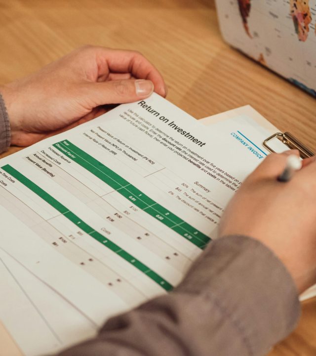 A person analyzing a return on investment report with a pen in hand on a desk.